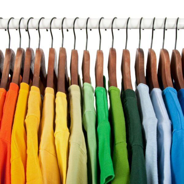Kleidung in Regenbogenfarben auf hölzernen Kleiderbügeln. #daskannkunststoff #sustainability