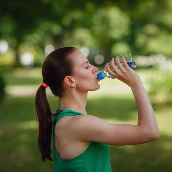 Junge dunkelhaarige Frau in grünem T-Shirt trinkt Wasser im grünen Park nach dem Training #daskannkunststoff #nachhaltigkeitimalltag